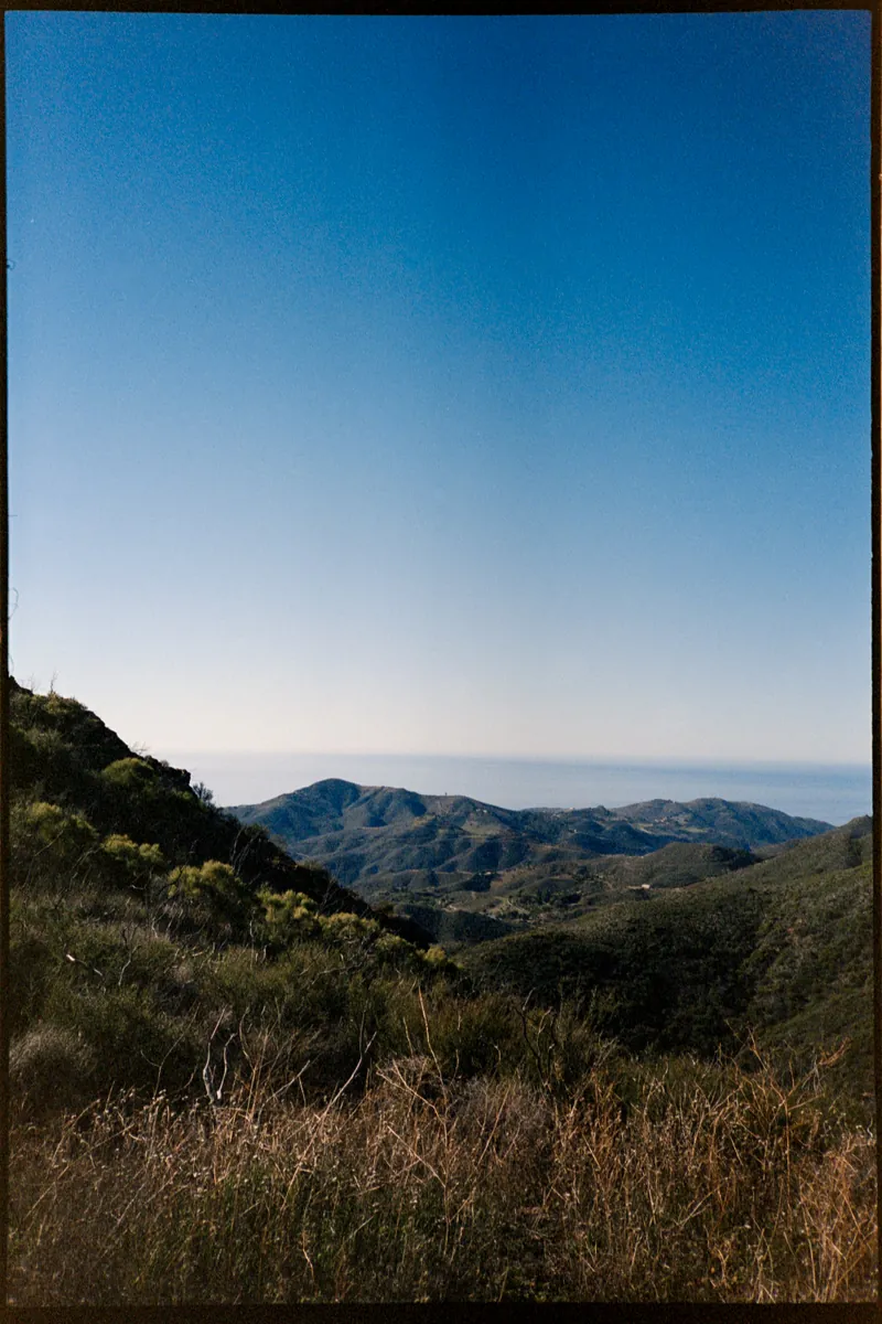 Malibu hills rolling down to the ocean under a clear blue sky, shot on film